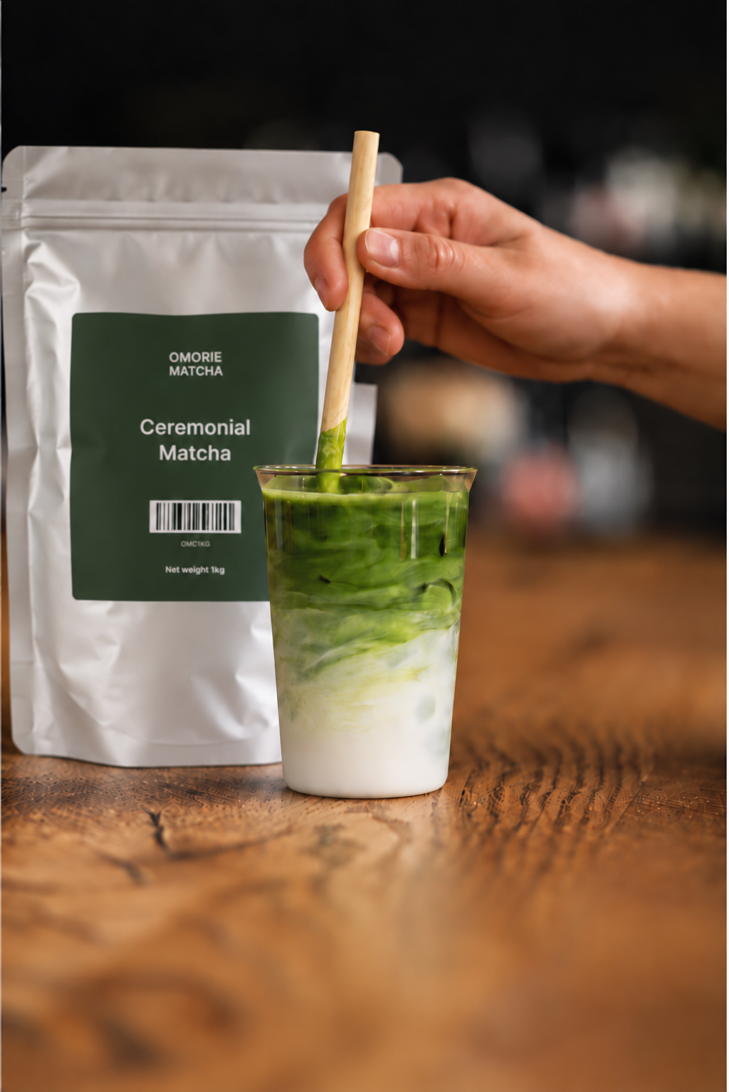 An iced matcha latte being stirred beside a bag of Omorie Ceremonial Matcha.